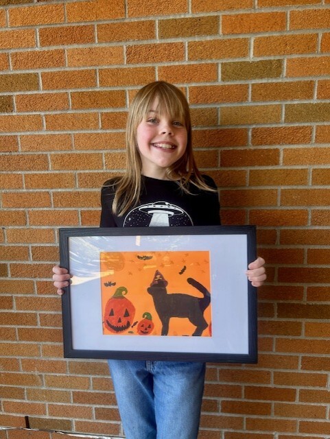 Smiling student with dark blonde hair holding a framed picture of a black cat and pumpkins.