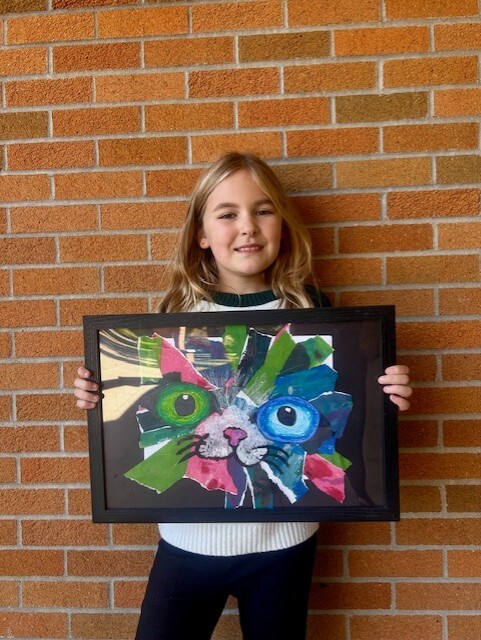 Blonde student holding a framed image of riped and cut layered papers created into a cat's face.