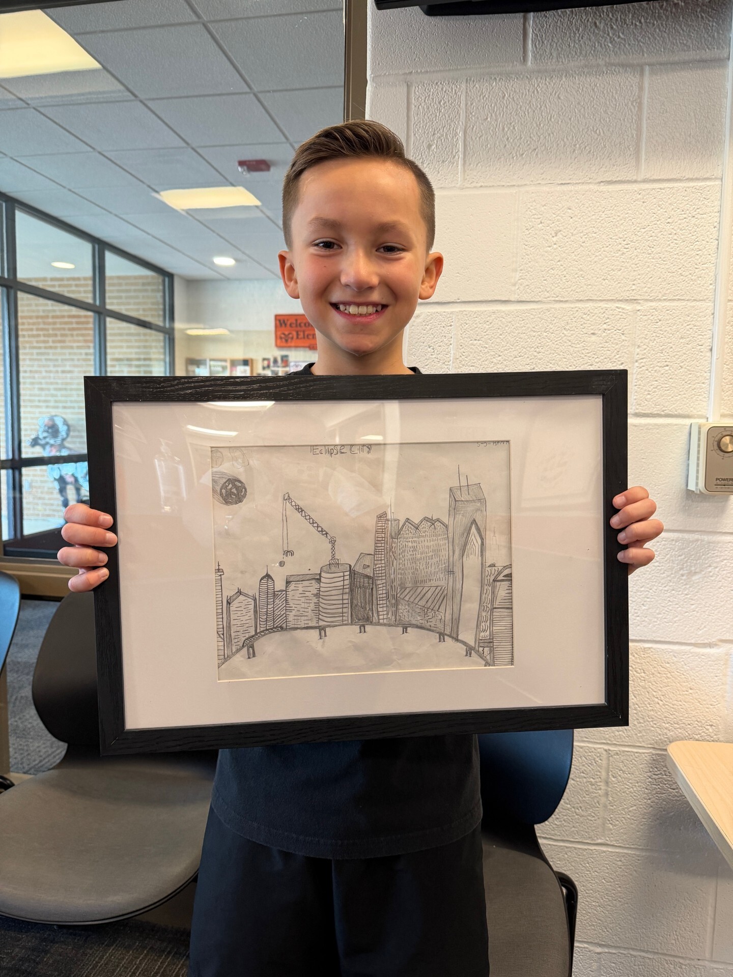 Student with brown hair smiles holding his framed artwork with a detailed city construction scene with a meteor flying in from the side.