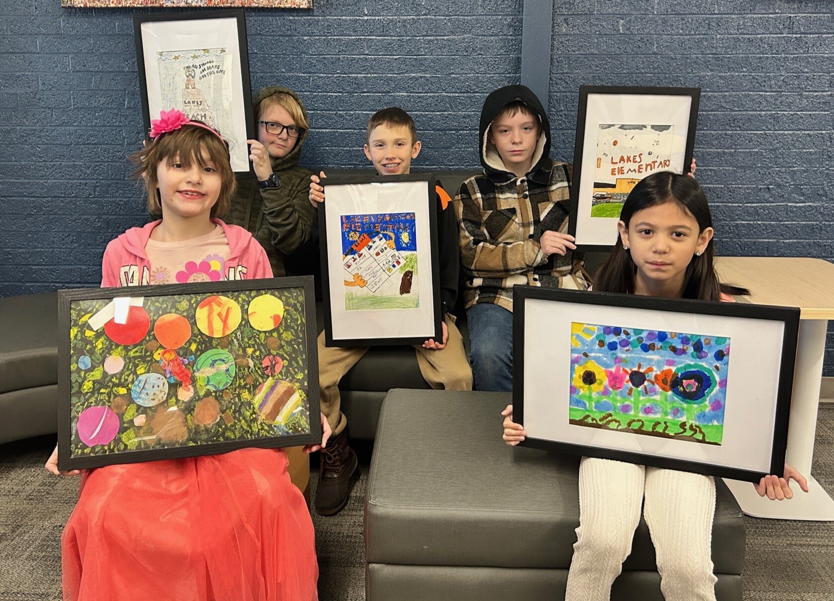5 students smiling while holding framed artwork