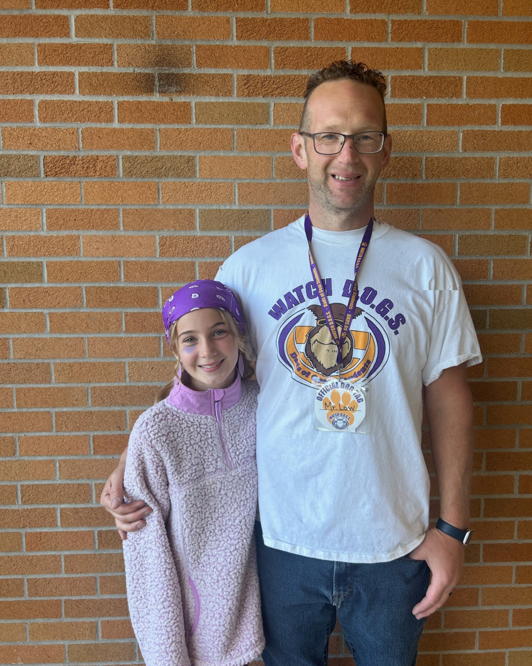 Student wearing lots of purple clothing stands next to a man in a Watch DOGS tshirt