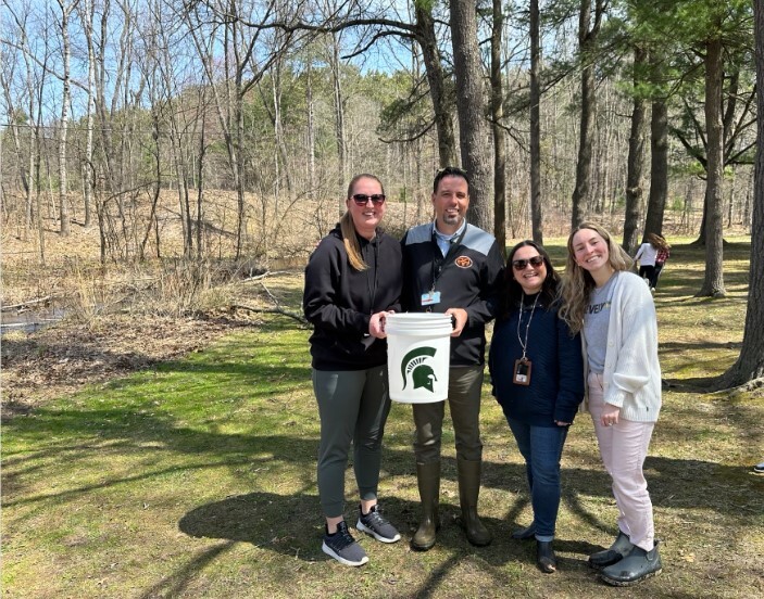 Mrs. Ejups, Mr. Zokoe, Mrs. Schirmann, and Mrs. Nelson stand by the water's edge