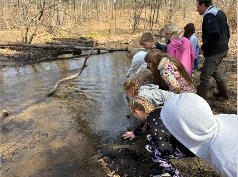 Students and principal Zokoe stand on the water bank watching the salmon swim away