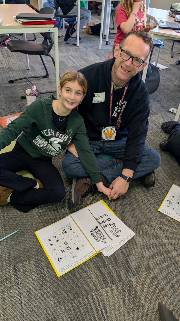 girl in green shirt with blond hair and man in black sweatshirt sitting on the floor and smiling at the camera