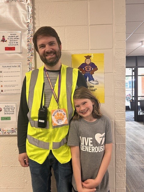 Dad in a yellow vest stands with his proud and smiling daughter