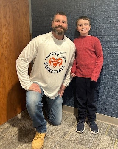 Image of a man kneel next to his son. Both are smiling
