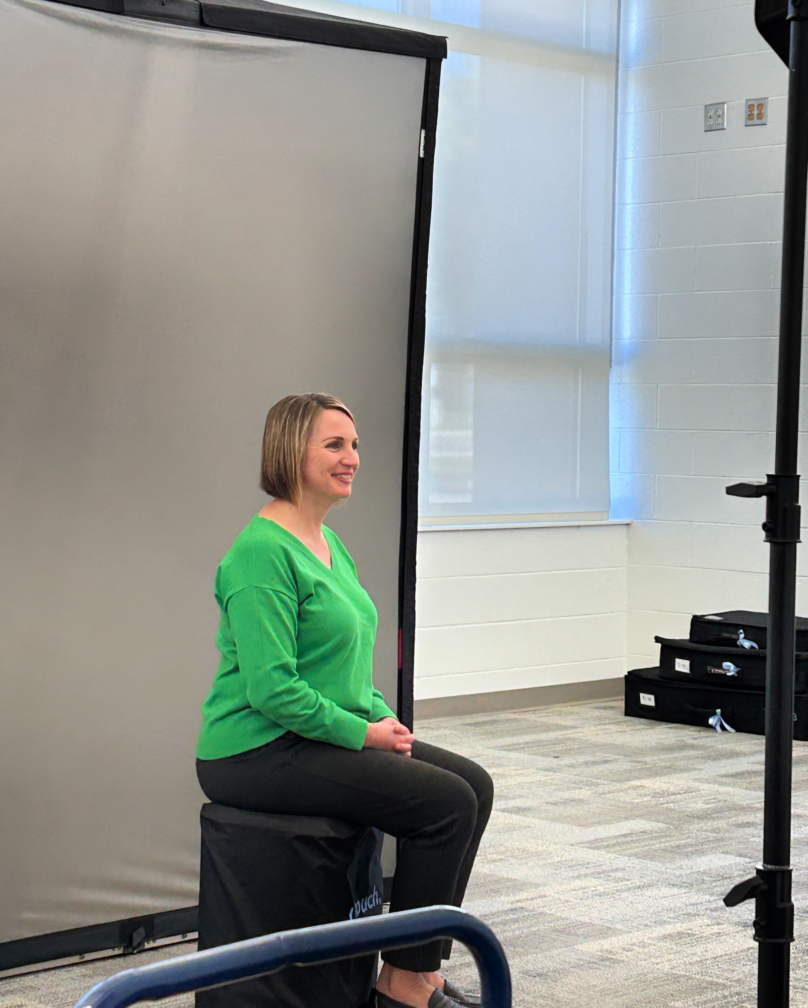 Mrs. McGinn smiles and sits in front of a screen while getting her picture taken by a school photographer.